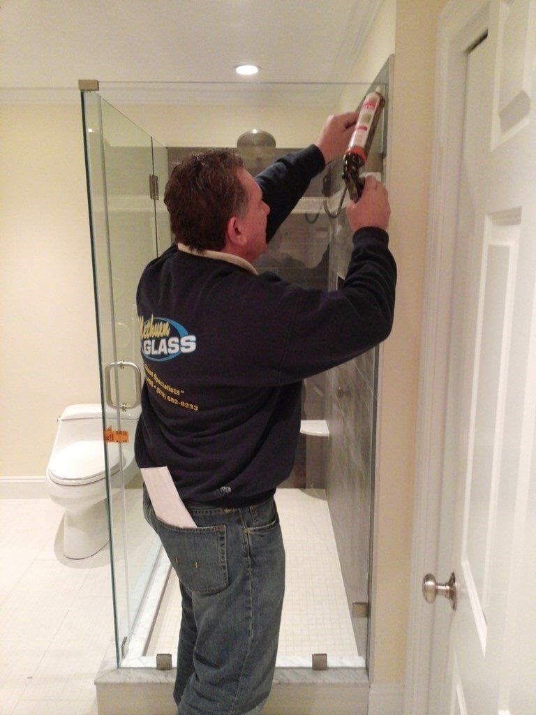 A man is installing a glass shower door in a bathroom.