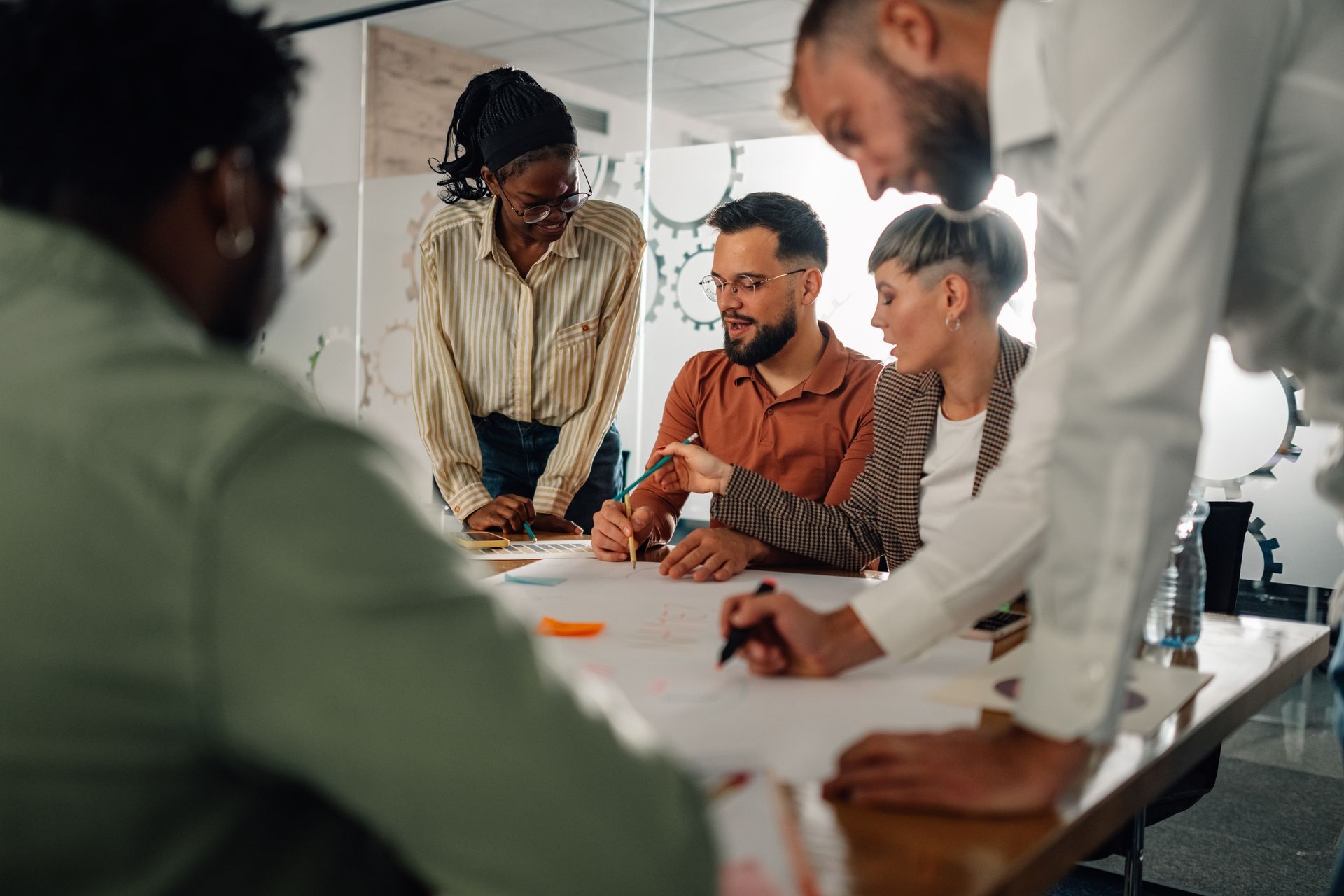 Team of people collaborating around a table, pointing at papers, indoors, focused discussion.