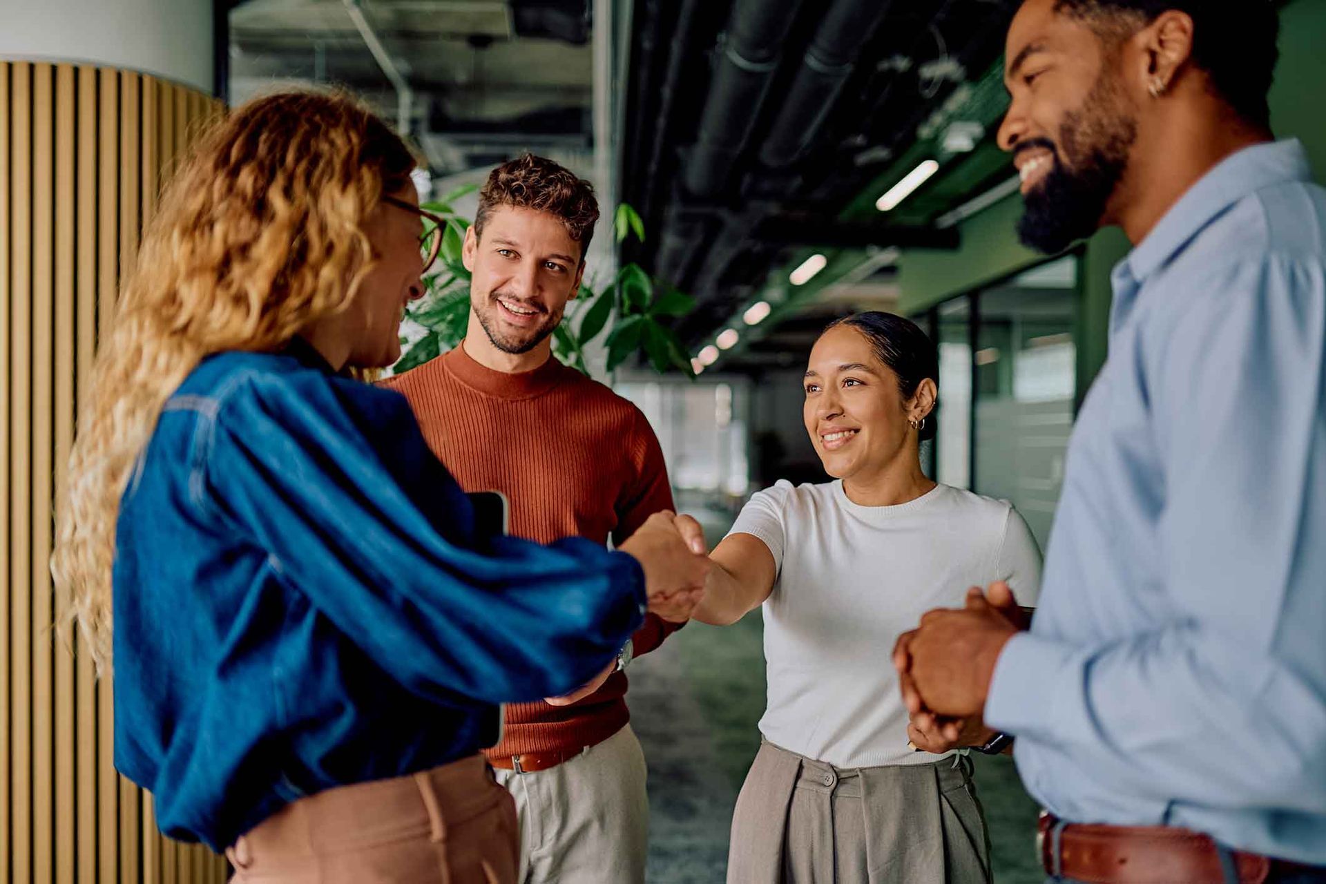 Four people in an office shake hands and smile. Two are in casual attire. Modern office setting.