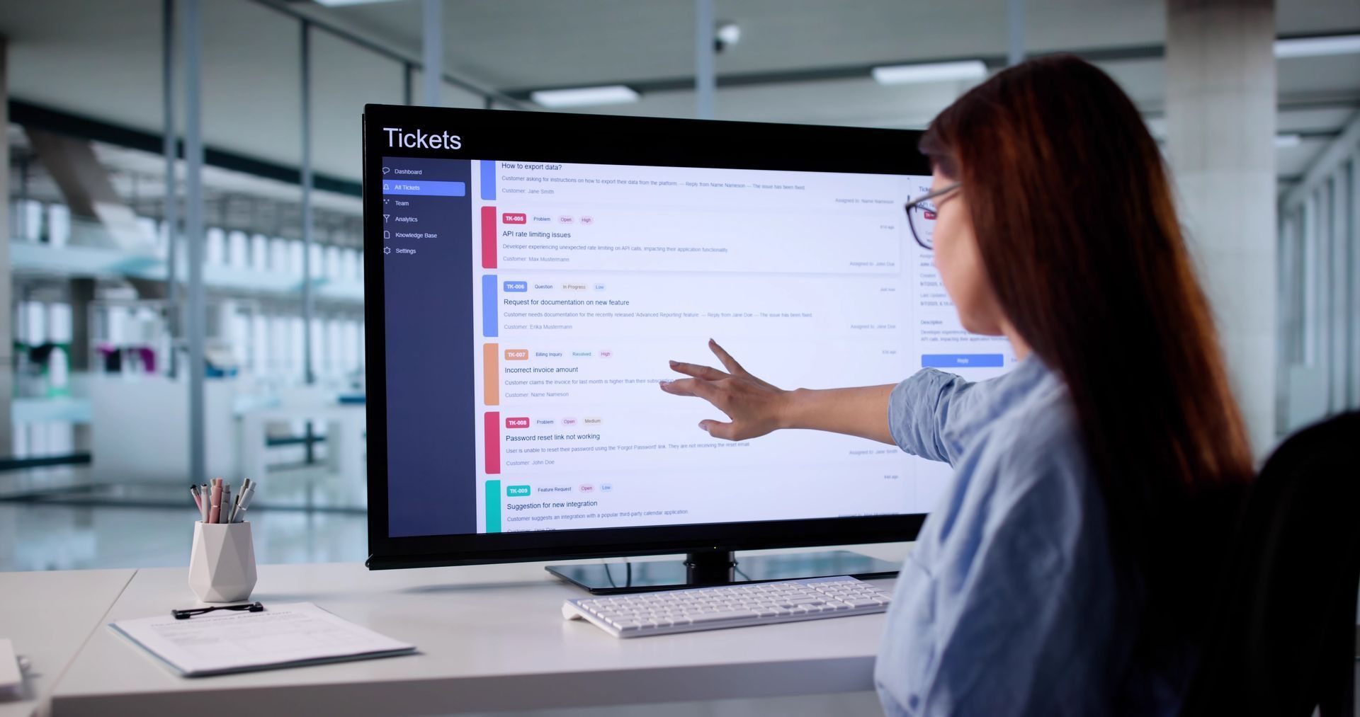 Woman pointing at a computer screen displaying a colorful user interface in an office setting.