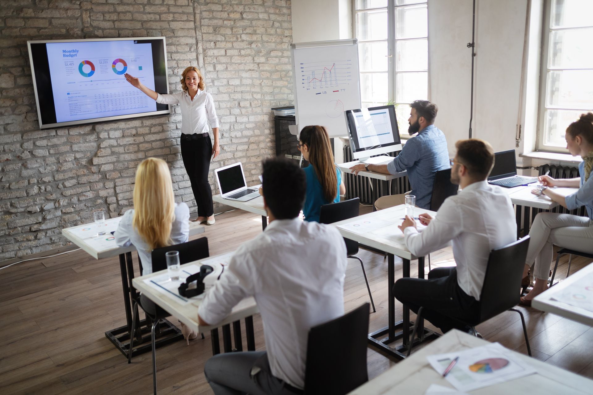 Woman presenting data on a screen to a group of people in a classroom.