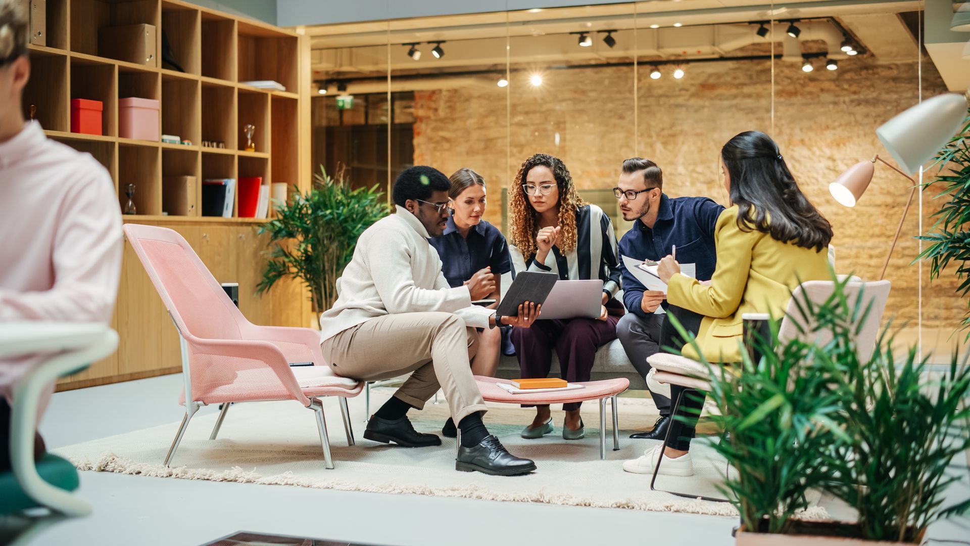 Group of people in an office meeting around a small table, discussing a tablet and papers.