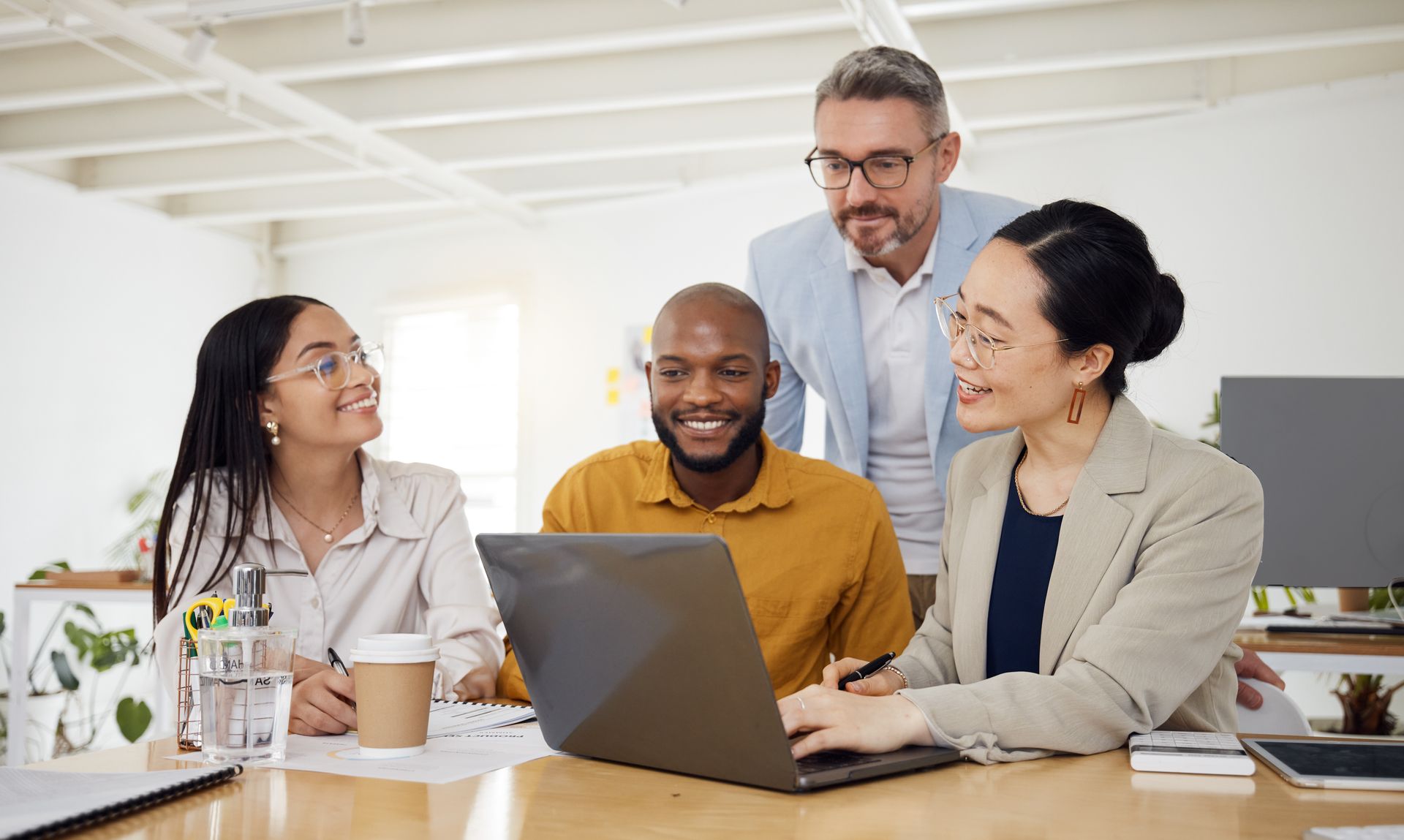 Four people at a table, looking at a laptop. They appear to be discussing something.