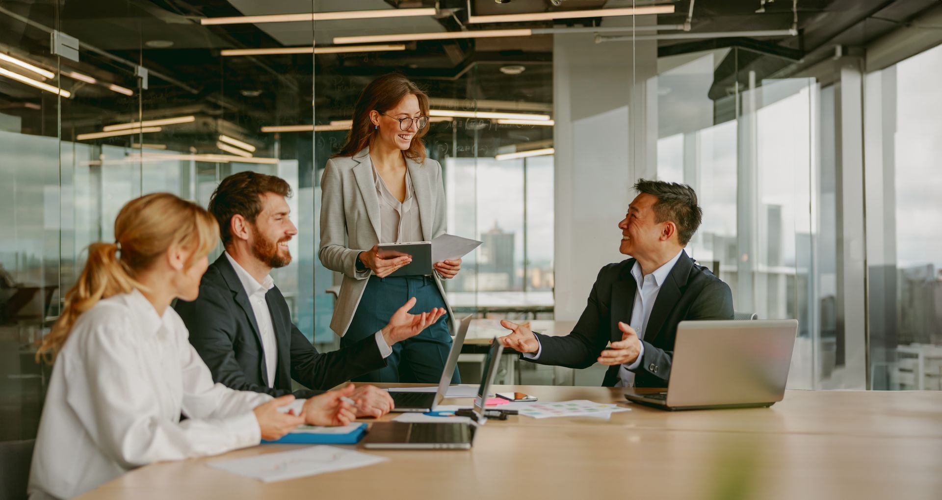 Four professionals in a modern office, one standing and presenting to seated colleagues.