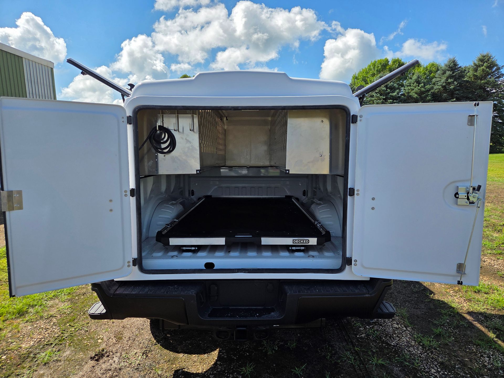 White truck bed with open doors, black interior, and a tray on the floor, outdoors.