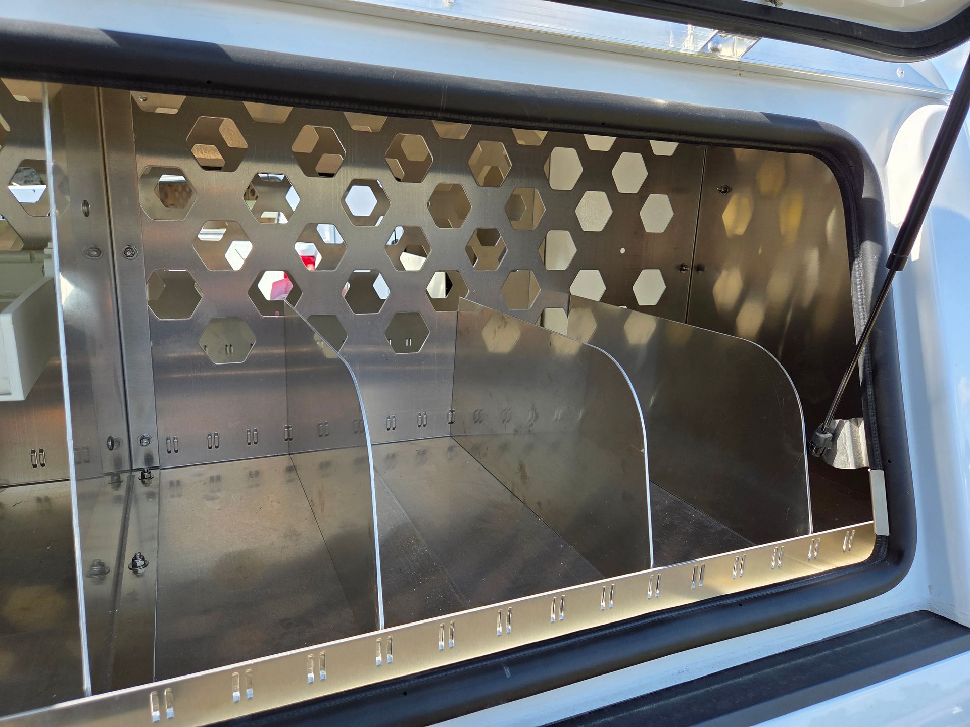 Metal storage compartment with dividers and honeycomb patterned vent.