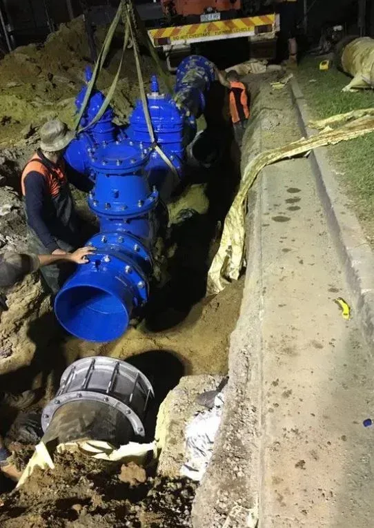 Workers installing a large blue water valve in a trench near a curb. A crane holds the valve — Far North Plumbing in Mourilyan, QLD