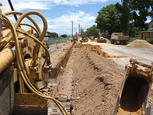 Construction site with trench being dug, equipment and workers on a road, clear sky — Far North Plumbing in Mourilyan, QLD