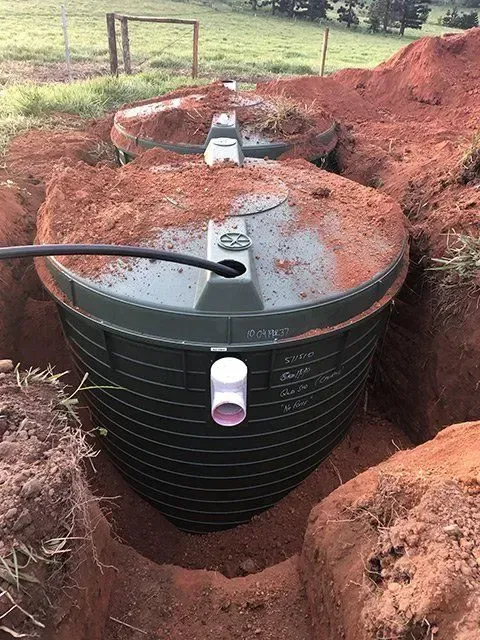 Two buried green septic tanks in an excavation, surrounded by reddish soil and grass — Far North Plumbing in Mourilyan, QLD