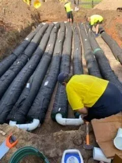 Workers Installing a Septic System With Black Drainage Tubes in a Trench — Far North Plumbing in Mourilyan, QLD
