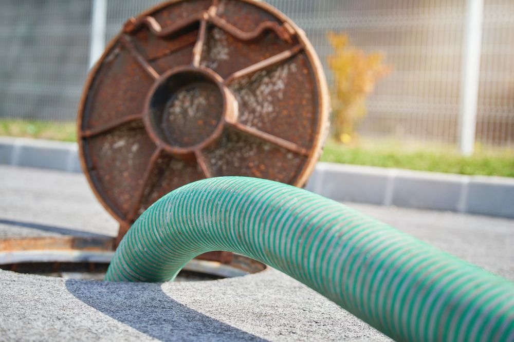 Green Hose Entering an Open Manhole With Rusty Cover — Far North Plumbing in Mourilyan, QLD