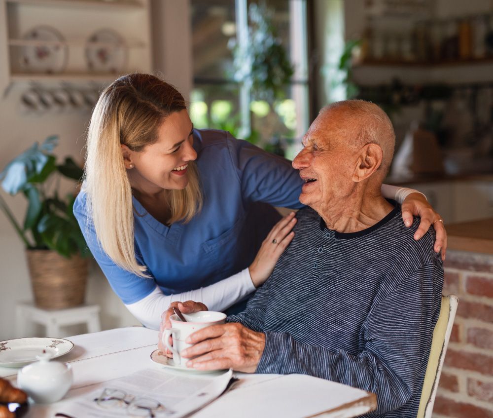 An Elderly Man is Sitting at a Table with a Nurse — Fishers, IN — Alluring Warmth Home Care LLC