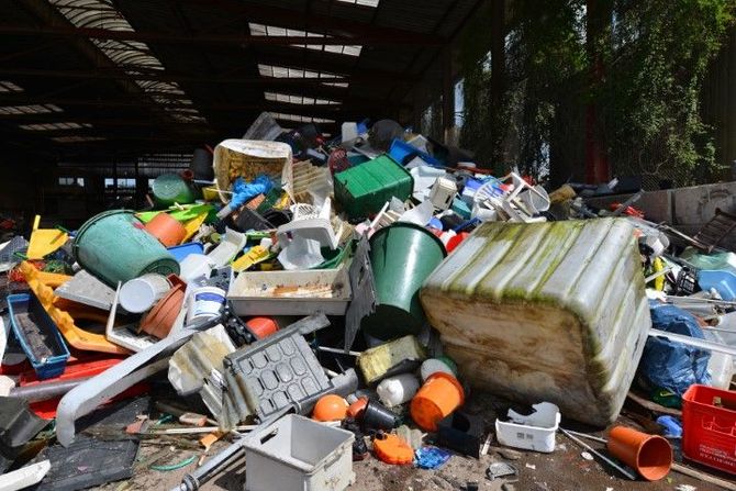 Overflowing pile of mixed trash and discarded containers in a dim, covered area