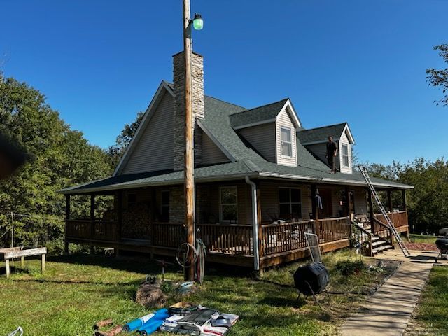 A house with a green roof and a porch is being painted.