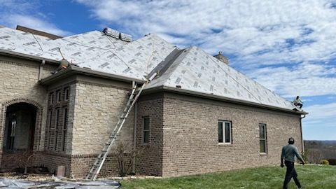 A man is walking in front of a brick house with a ladder attached to it.