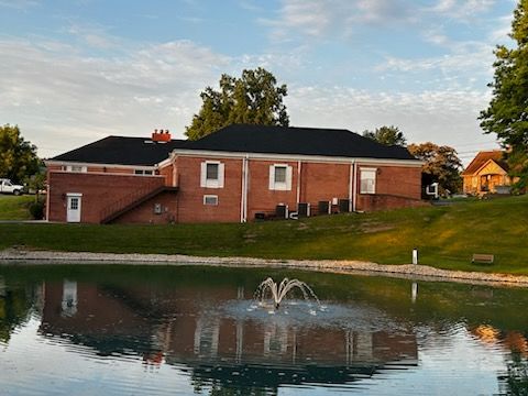 A brick house sits next to a pond with a fountain in front of it