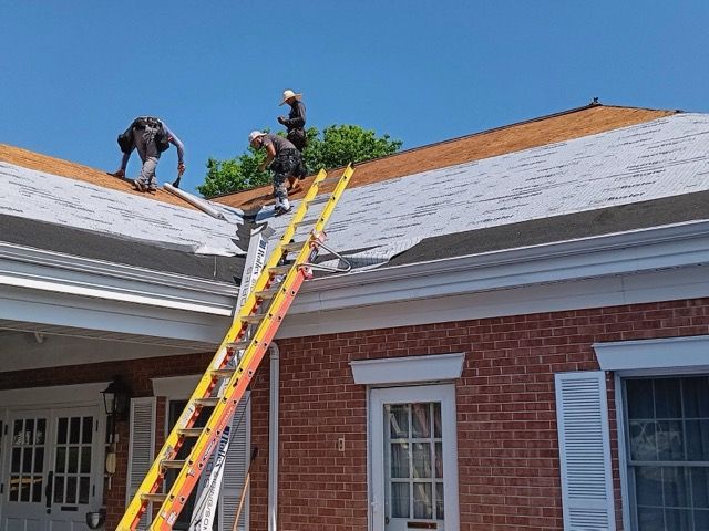 Two men are working on the roof of a brick house.