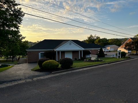 A brick house with a black roof is sitting on the side of the road.