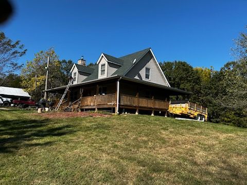 A large house with a large porch is sitting on top of a lush green hill.
