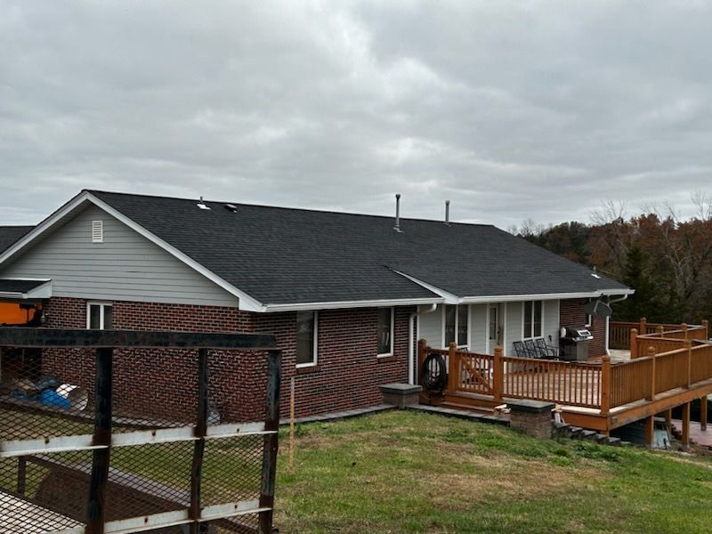 A brick house with a black roof and a wooden deck.