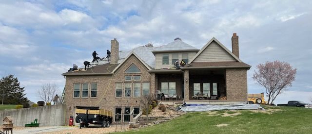 A large brick house with people working on the roof.