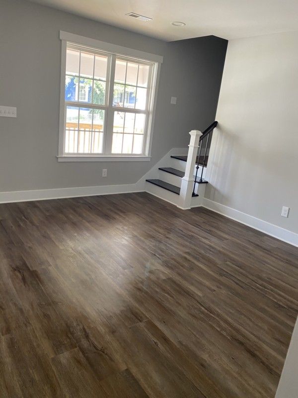 Empty room with dark wood floors, gray walls, a window, and a small staircase.