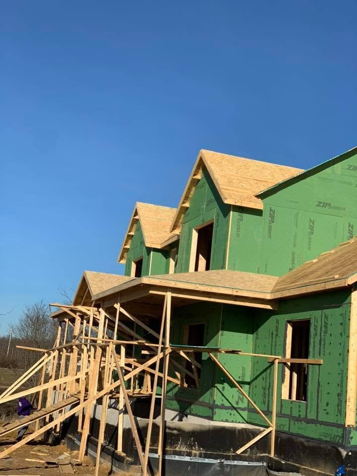 Green house under construction with wooden scaffolding and a partially finished roof against a blue sky