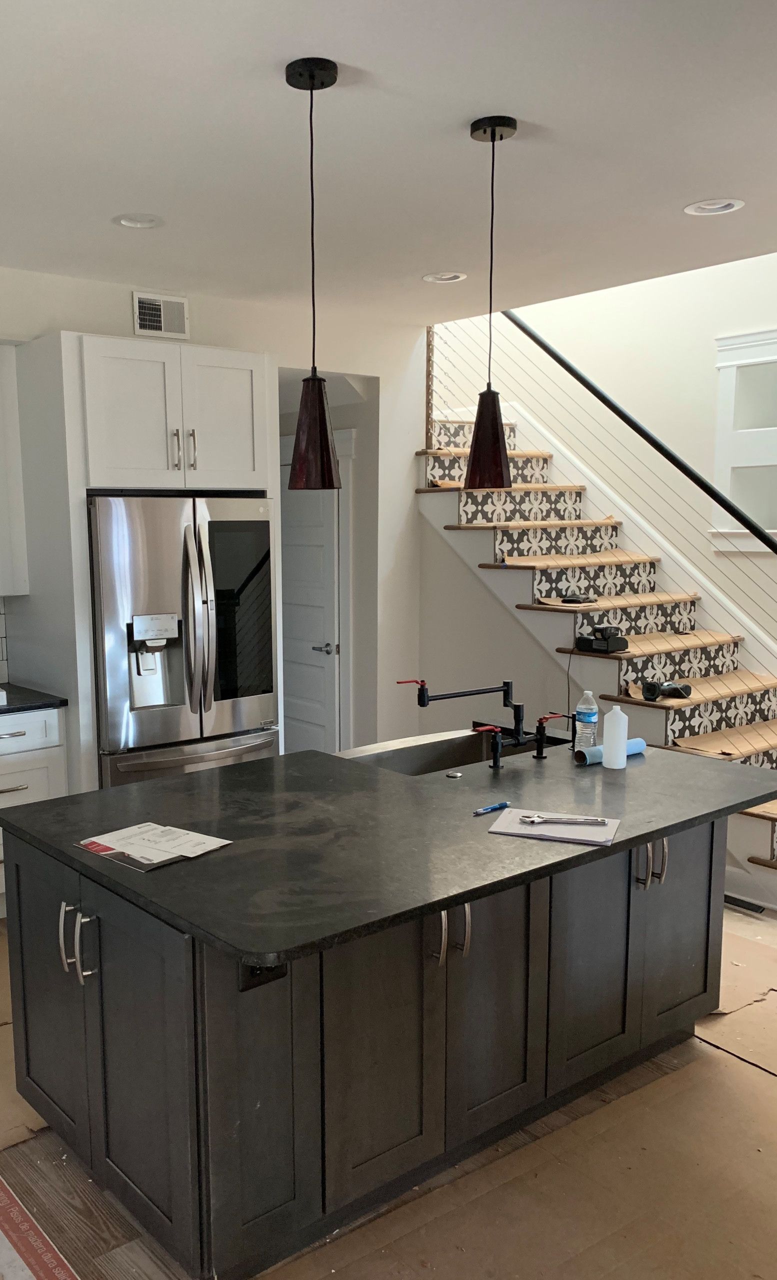 Modern kitchen with dark island, stainless fridge, and staircase with patterned runner in background