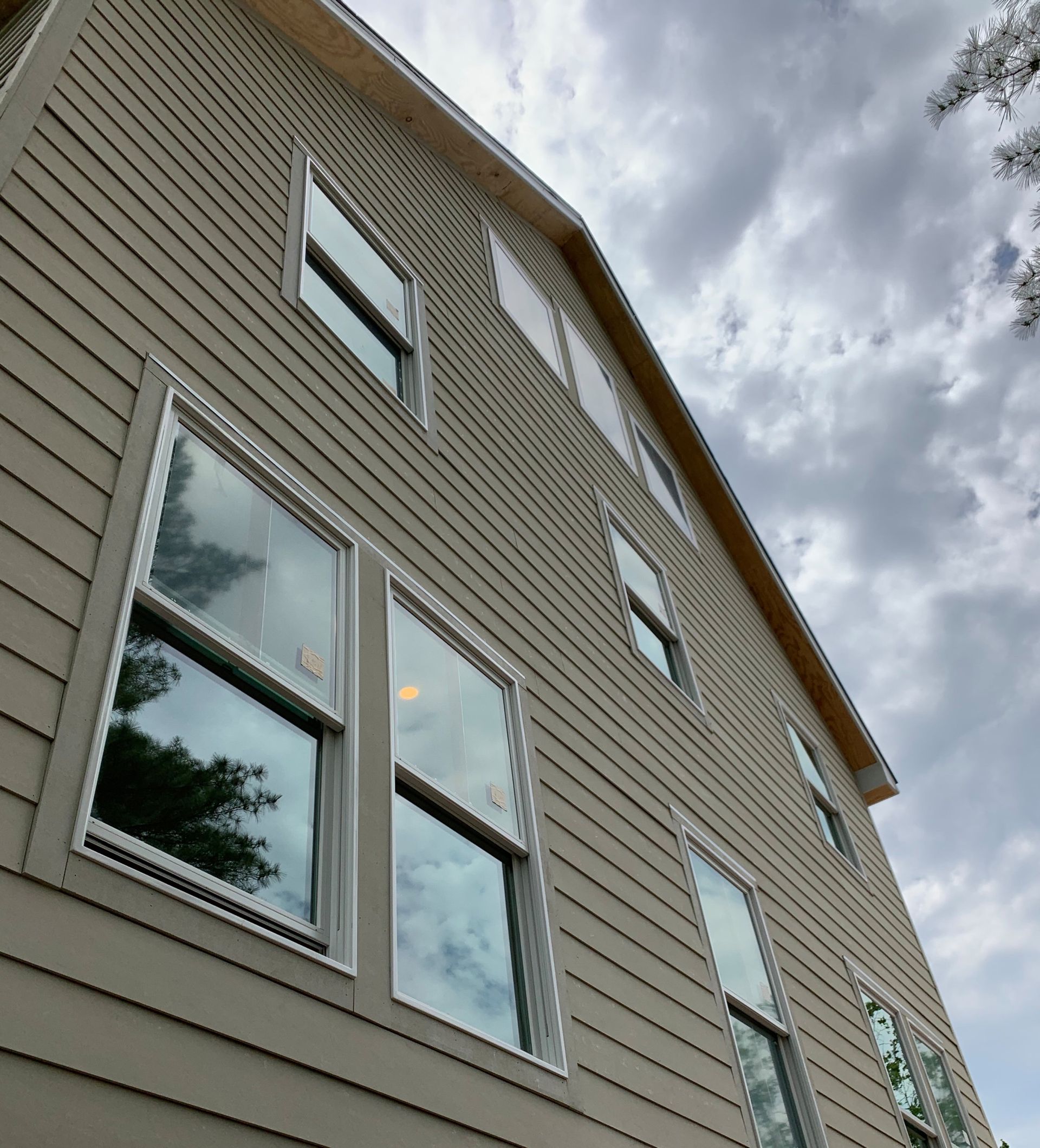 Upward view of a beige house exterior with several windows against a cloudy sky