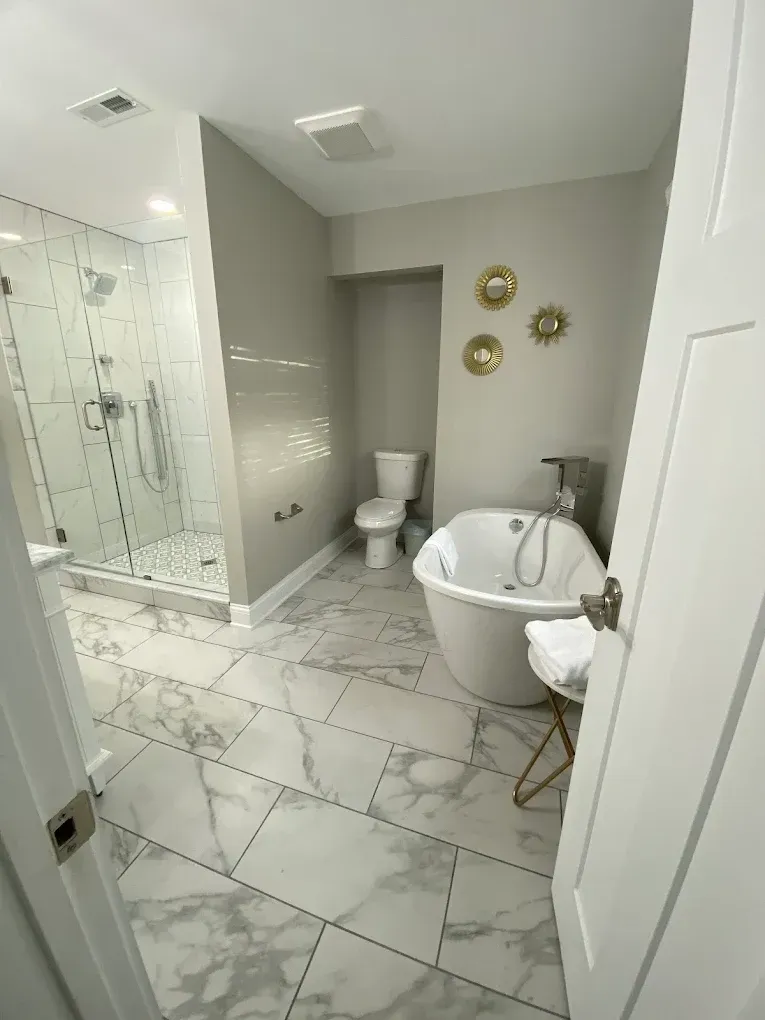 Modern white bathroom with glass shower, toilet, and freestanding tub on marble-pattern tile floor