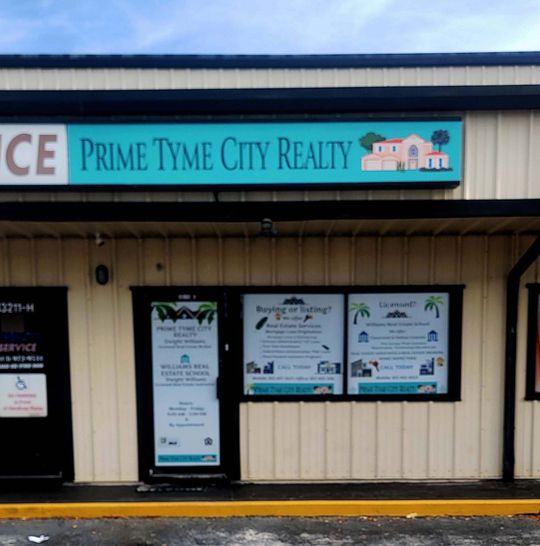 Exterior of Prime Tyme City Realty storefront with sign, doors, and window displays. Turquoise, beige, and black colors.