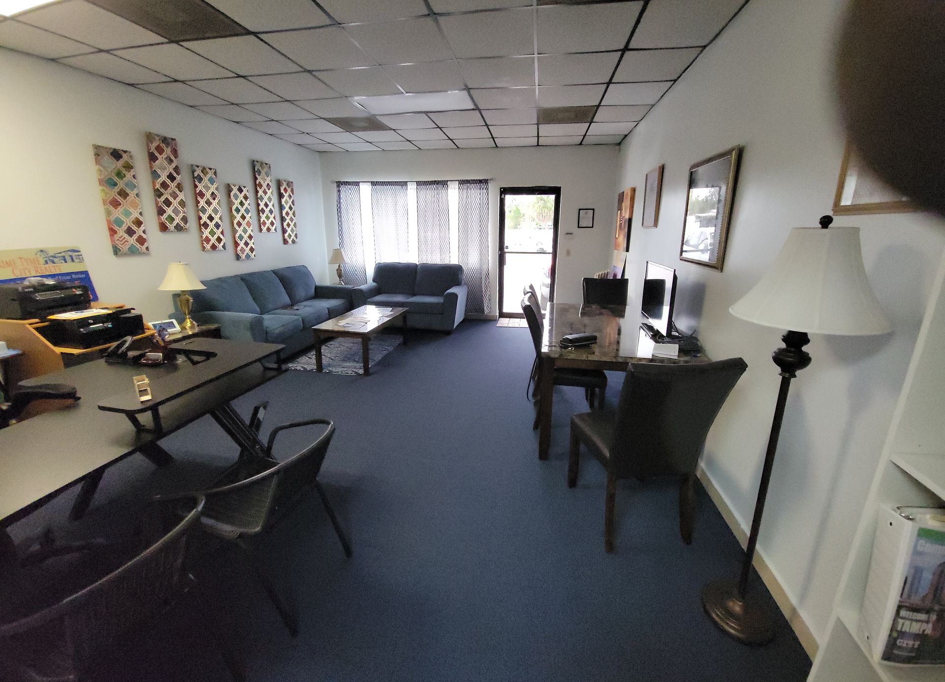 Interior office space with blue carpet, couches, desks, computers, and decorative wall art.