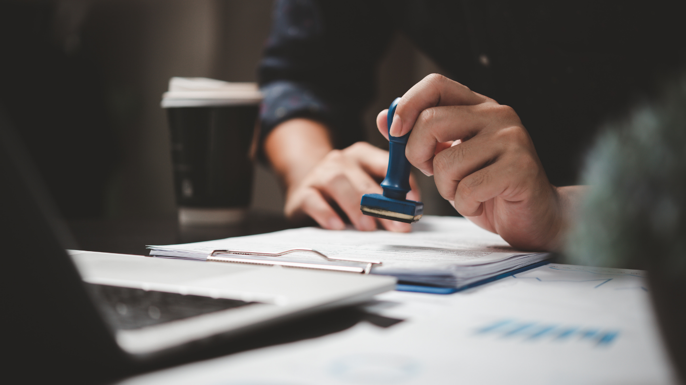 Person stamping a document on a desk with a laptop and charts.