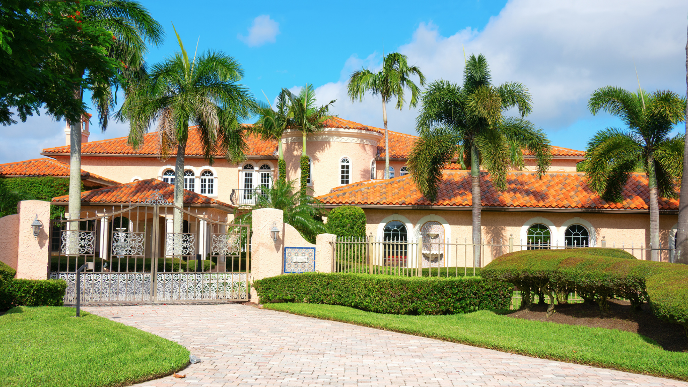 Small, light green house with white trim, front porch, and brick accents, under a clear blue sky.