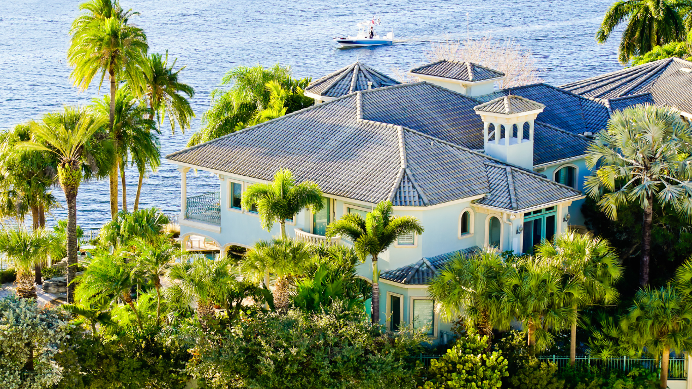 Tan single-story house with stone facade, white garage door, and green shutters on a sunny day.