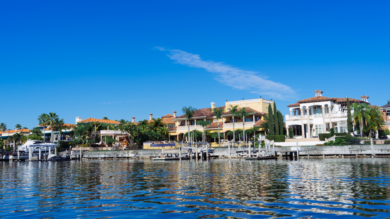 Modern home with glass walls, outdoor seating, and lush greenery.