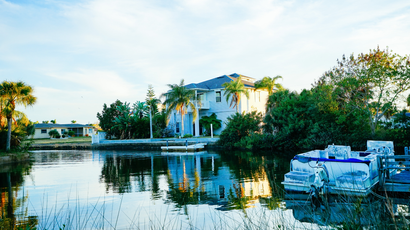 Sunset over calm water with palm trees, clouds, and orange, pink, and blue hues.