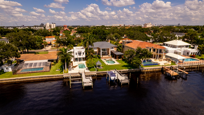Modern two-story house with a carport, large windows, and gray and white exterior, set in a landscaped yard.