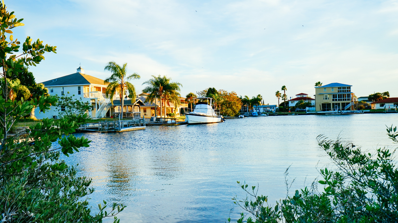 Tan brick house with a driveway surrounded by green grass and trees.