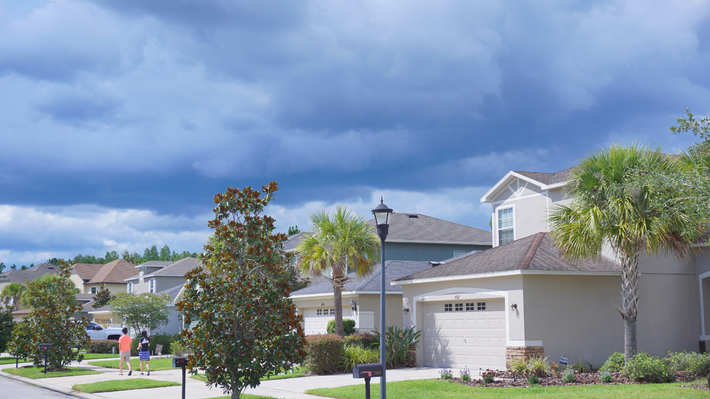 Two-story gray house with white trim, porch, and attached garage; set on a grassy hill with trees.