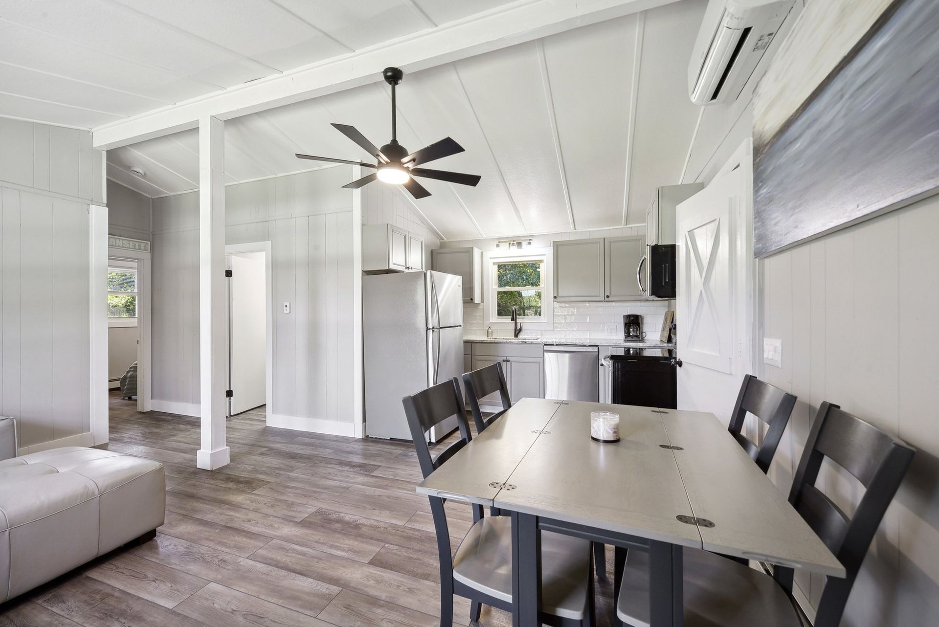 A bright, open-plan kitchen and dining area with gray wood-look flooring, a gray table, and a ceiling fan.