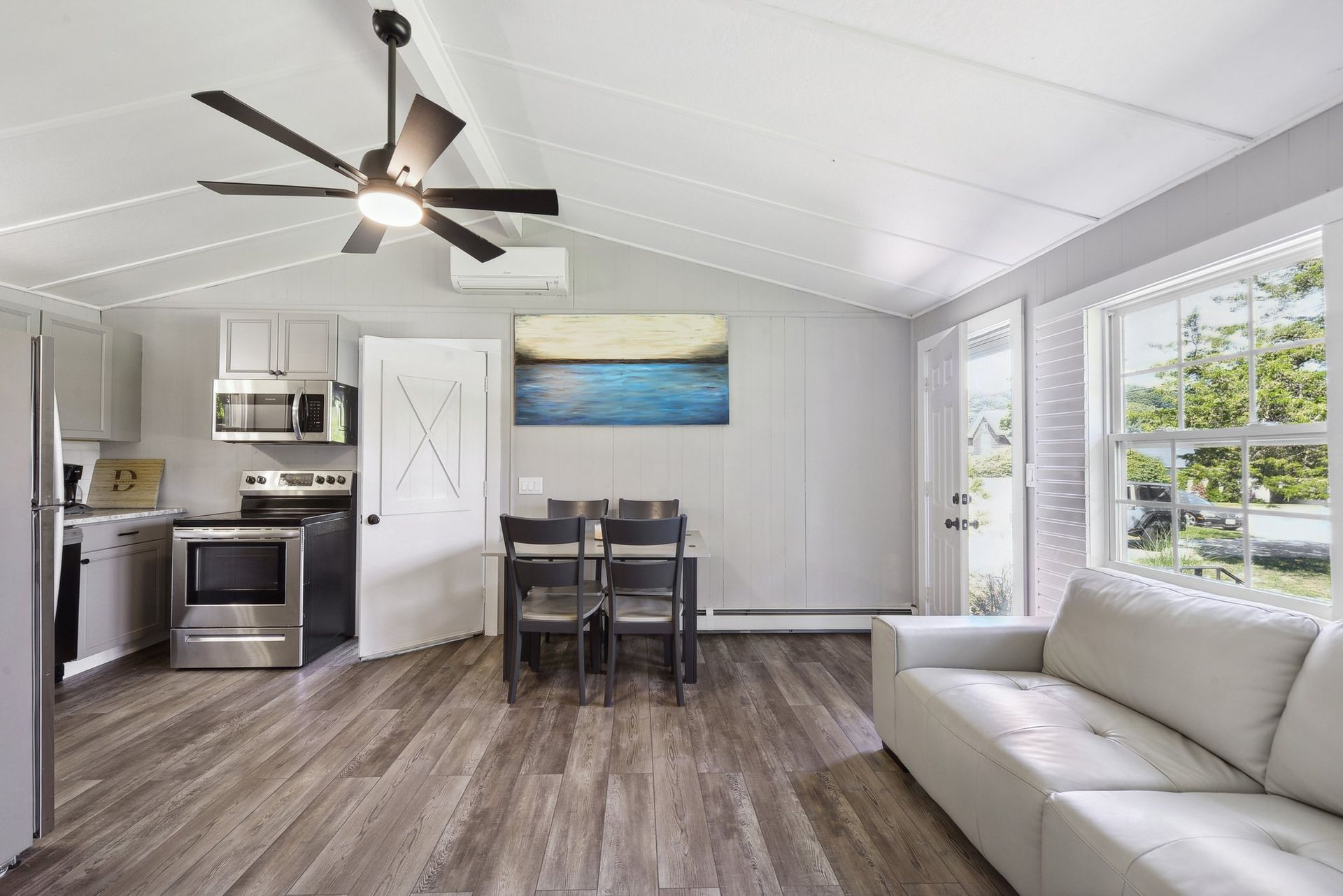 A modern, open-concept living area featuring a kitchen, dining table, and a light-colored couch on wood-look flooring.