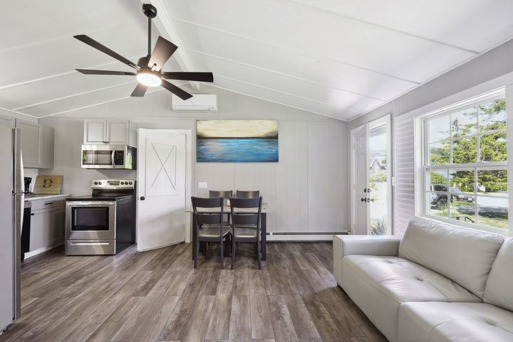 A modern, open-concept living area featuring a kitchen, dining table, and a light-colored couch on wood-look flooring.