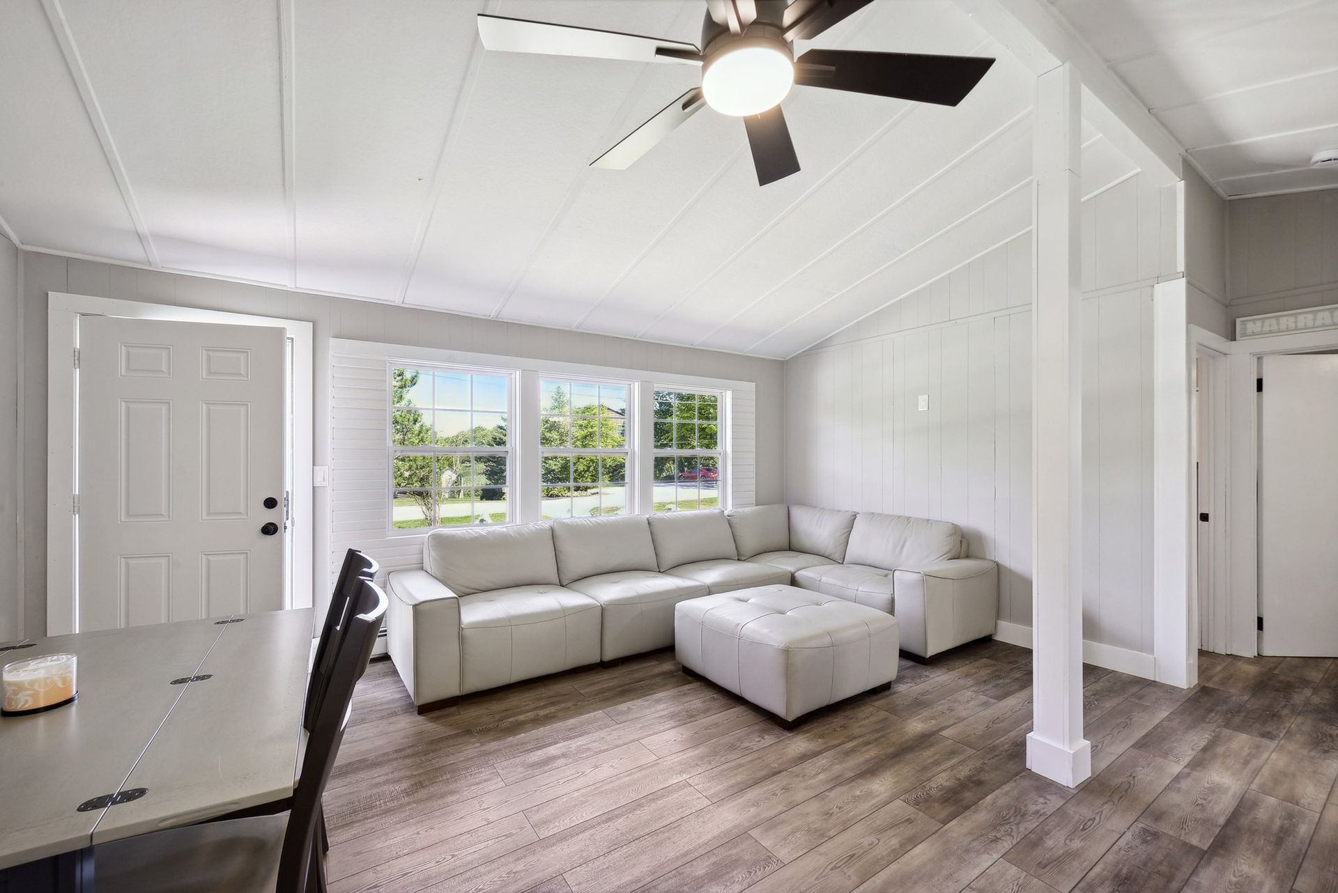 A bright living room with white walls, a gray sectional sofa, a matching ottoman, and wood-look floors.