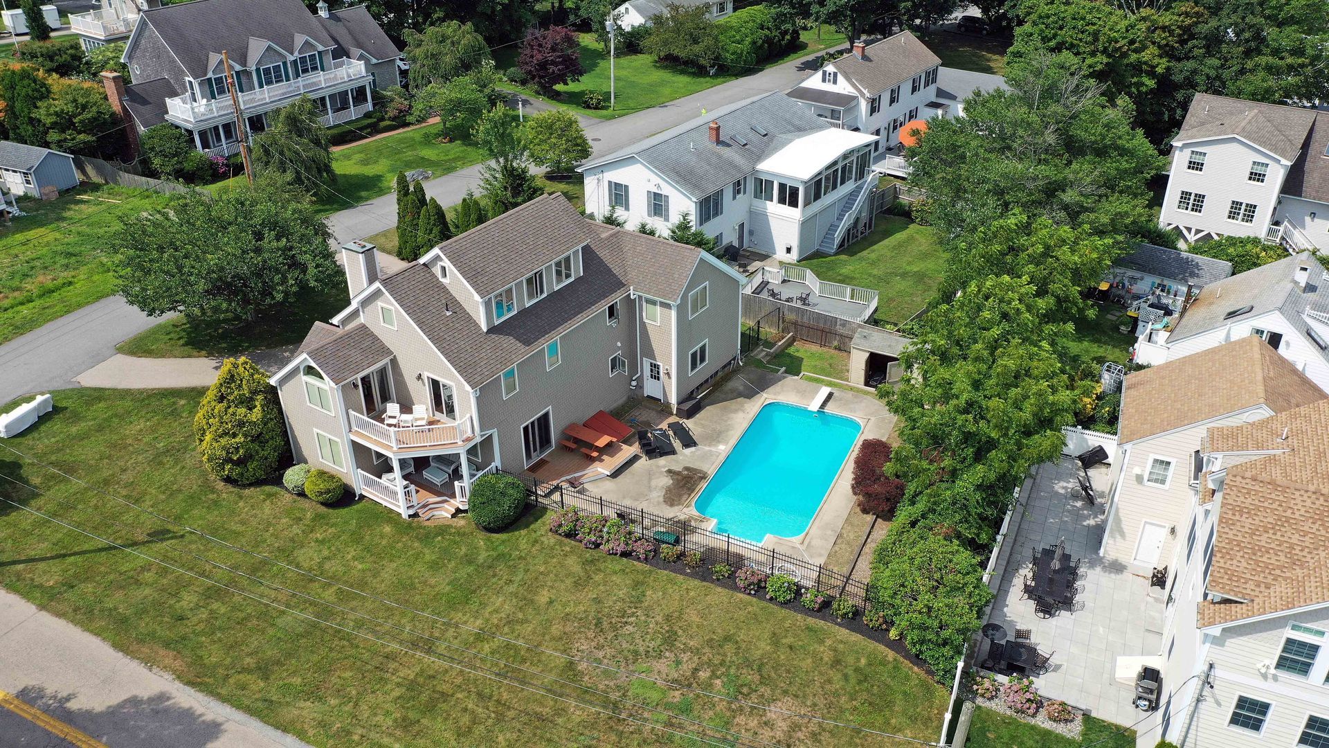 Aerial view of a gray suburban house with a backyard swimming pool and surrounding residential neighborhood.