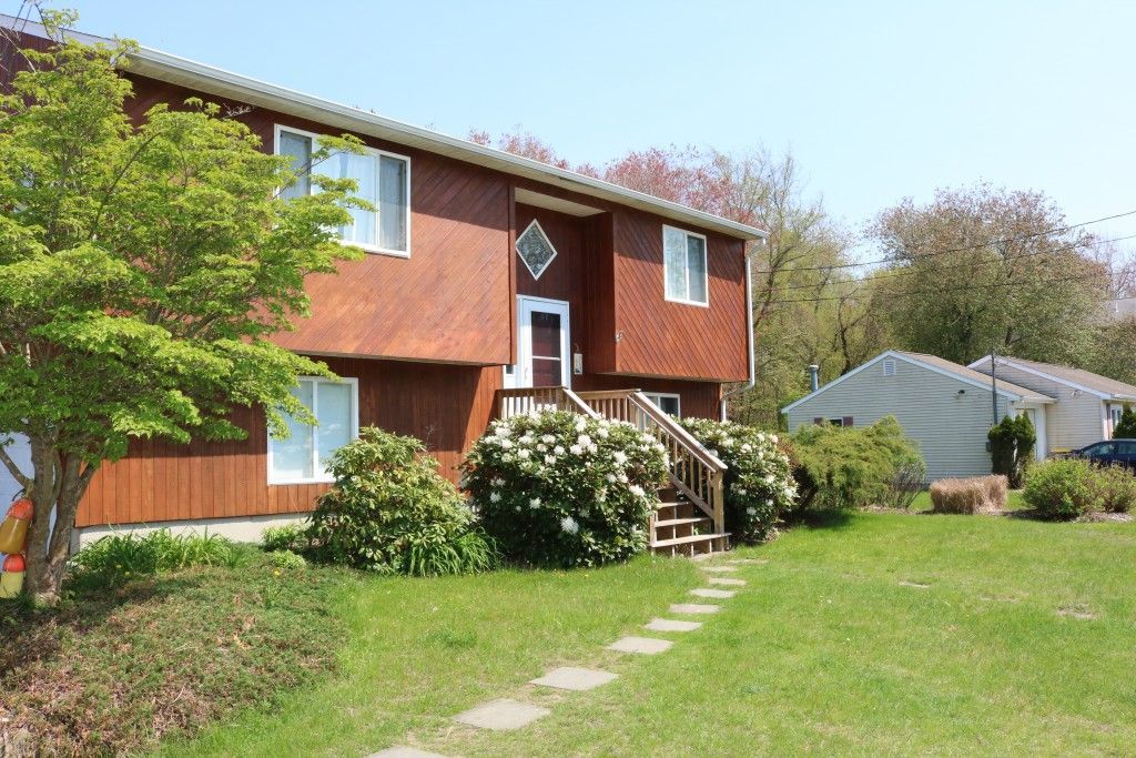 A two-story brown house with white trim and a stone path leading to the front stairs, surrounded by trees and bushes.