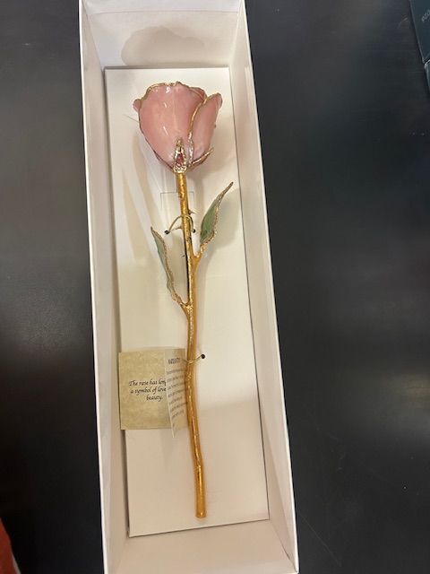 Pink and gold rose in a white box. The stem and leaves are gold. There is a small tag on the stem.