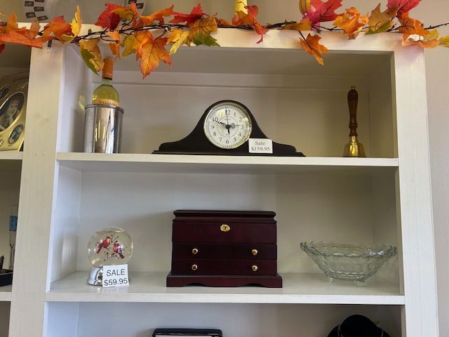 White shelves display a clock, jewelry box, snow globe, and other items, decorated with autumn leaves.