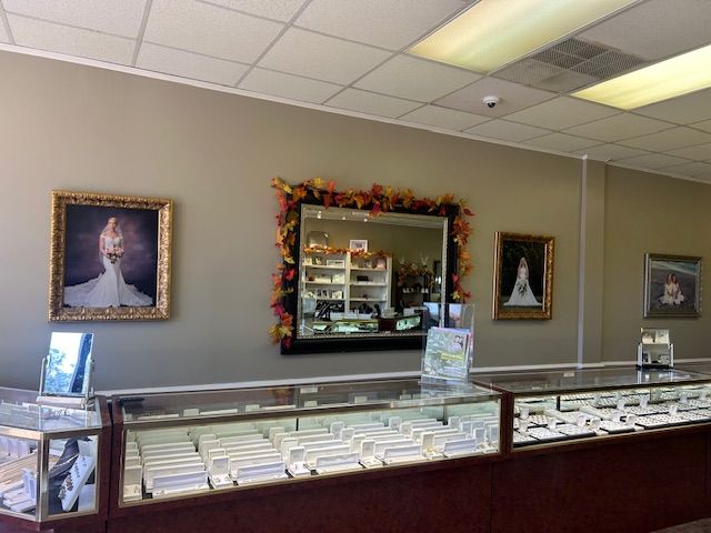 Jewelry store interior with display cases, mirrors, framed portraits, and beige walls.