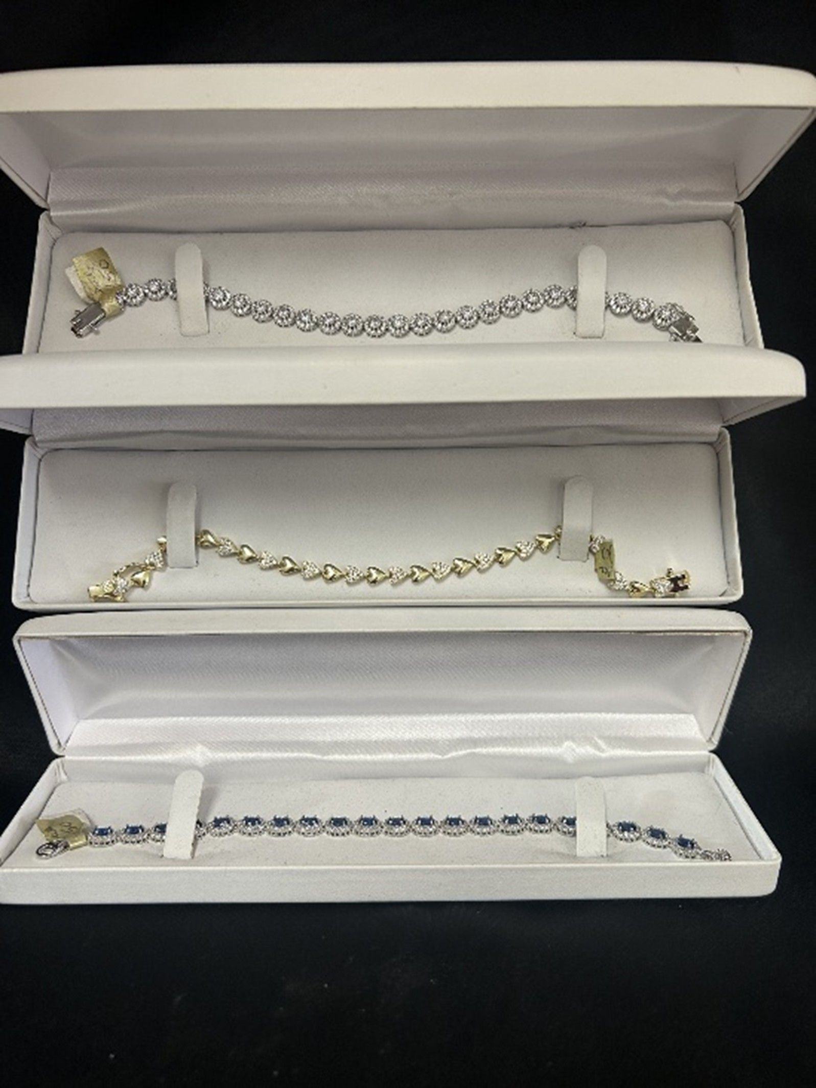Three open white jewelry boxes, each holding a different gemstone bracelet.
